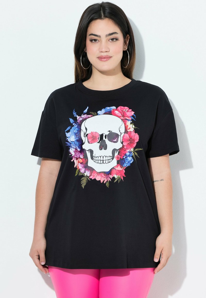 Sort bomulds t-shirt med et stort kraniegrafik indrammet af levende blomsterdesigns i pink, blå og grøn. Korte ærmer, afslappet pasform.