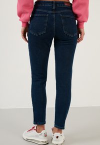 Modre skinny jeans iz denima z visokim pasom, zadnjimi žepi in rahlo zbledelim dizajnom. V kombinaciji z belimi in rdečimi športnimi čevlji.