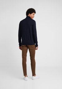 Marineblauwe trui met lange mouwen en hoge kraag, gecombineerd met bruine strakke broek en witte sneakers; soepele textuur en casual stijl.