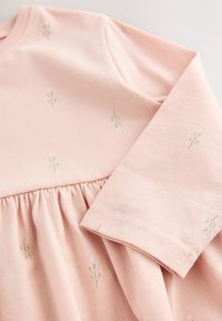 Svetloružové šaty z mäkkej bavlny, s nariaseným pásom a drobnými zelenými kvetinovými vzormi po celej ploche. Dlhé rukávy s dokončenými lemami.