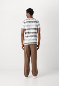 Camiseta de manga corta con franjas horizontales grises y blancas sobre un fondo claro. Combinada con pantalones de pierna ancha marrones y zapatillas.
