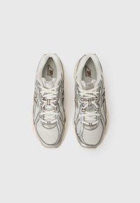 Pari valkoisia ja harmaita New Balance -juoksukenkiä nauhoilla, katsottuna ylhäältä valkoista taustaa vasten.