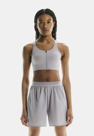 Sportivo grigio chiaro con zip frontale e spalline larghe abbinato a pantaloni corti leggeri con vita elasticizzata.