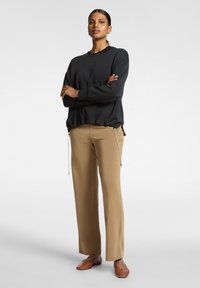 Schwarzer Pullover mit strukturiertem Design vorne, kombiniert mit beigen Hosen mit metalldetails am Kordelzug und lockerem Schnitt. Braune Ballerinas.