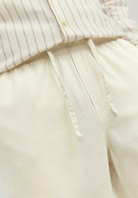 Light beige, soft fabric pants with an elastic waistband and drawstring. Features a relaxed fit and minimal texture for comfort.
