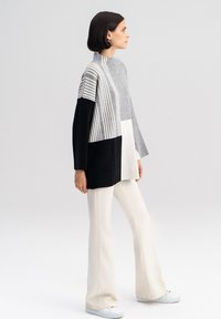 Gebreide pullover met een hoge hals; bevat grijze, zwarte en crèmekleurige secties met verticale strepen. Gecombineerd met crèmekleurige flared broek en witte schoenen.