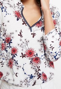 Weißes Langarmshirt mit floralem Muster in Rot und Marineblau, einem marineblauen Ausschnitt und einer weichen Haptik.