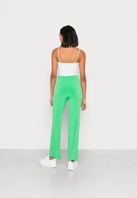 Calças largas verdes feitas de um tecido suave e elástico, combinadas com uma blusa justa branca. Ténis brancos completam o visual.
