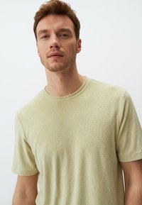 Jasnozielona koszulka z krótkim rękawem, okrągły dekolt, miękka tekstura, lekko luźny krój, minimalne wykończenia, prosty design bez wzorów.