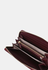 Portafoglio in pelle bordeaux con zip dorata, molteplici scomparti per schede e una tasca centrale con zip. Texture liscia con un design strutturato.