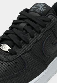 Crne Nike Air Force 1 tenisice s teksturiranom kožnom gornjom, ravnim crnim vezicama, suptilnim brandom i bijelim međuslojem.