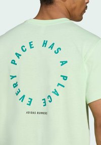 Light green cotton T-shirt featuring circular text in turquoise, reading "EVERY PACE HAS A PLACE," with "ADIDAS RUNNERS" below.