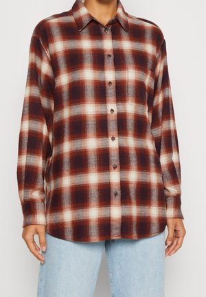 Chemise flanelle à carreaux rouges et bruns avec un col, des manches longues et un devant à boutons ; présente une texture douce et un dégradé subtil dans les couleurs.