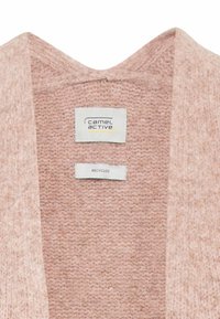 Vêtement en maille rose doux avec étiquette de marque « camel active » et une plus petite étiquette en tissu « recycled » sous l'encolure.