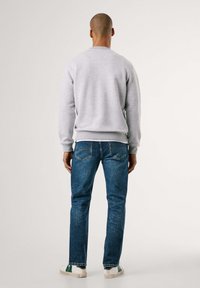 Sudadera de cuello redondo gris claro, jeans de mezclilla y zapatillas blancas con acentos verdes. Modelo de espaldas, mostrando los detalles del atuendo casual.