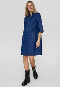 Jeansklänning med dragkedja i halsen, korta ärmar, två påsydda fickor, kontrasterande sömmar och rak passform. Buren med knähöga svarta stövlar.