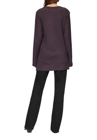 Langarm-Pullover in lila mit Rippenstruktur und Rundhalsausschnitt, kombiniert mit schwarzen Slim-Fit-Hosen. Der Stoff wirkt weich und hat eine dezente Textur.