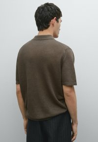 Krátký rukáv, hnědý polo tričko vyrobené z měkké tkaniny, s klasickým límcem a volným střihem, doplněné proužkovanými kalhotami.