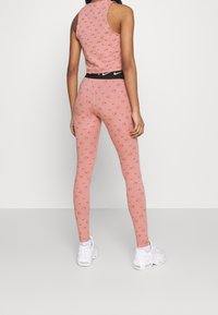 Rosa träningsset med en ärmlös topp och leggings. Mönstrad med små röda cirklar. Svart midja med en vit logotyp. Vita sneakers.