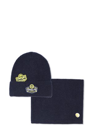 Bonnet en tricot côtelé bleu marine et chauffe-cou assorti, tous deux ornés de patches jaunes du logo Timberland.