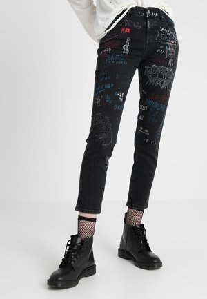 Černé úzké džíny s barevnými grafickými texty a kresbami, doplněné černými vojenskými botami a síťovanými ponožkami.