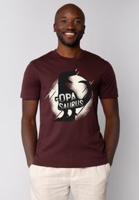 Bordeaux-rode t-shirt met een grafisch ontwerp dat een zwarte dinosaurus-silhouet toont en de tekst "OPA SAURUS," afgebeeld op een abstracte witte achtergrond.