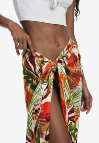 Gonna avvolgente floreale con vivaci motivi tropicali in rosso, verde e giallo, legata in vita, con uno spacco laterale per un tocco di stile.