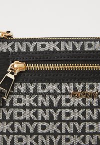 Mustvalge DKNY tõmmatav kotike, millel on logo trükk, kuldne riistvara ja tekstureeritud viimistlus. Kompaktne disain koos toimiva tõmblukuga.