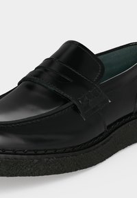 Μαύρο δερμάτινο παπούτσι τύπου penny loafer με ραμμένες λεπτομέρειες και χοντρή υφή στην σόλα, εμφανίζεται σε γωνιακή κοντινή λήψη.