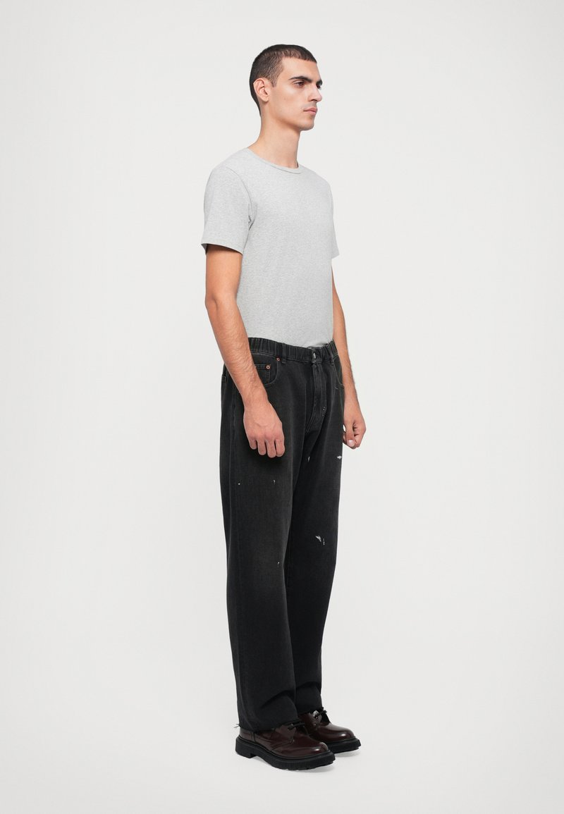 Gray short-sleeve t-shirt paired with black, loose-fit jeans featuring distressed accents. Model wears brown lace-up shoes.
