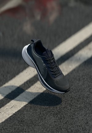 Scarpa sportiva grigio scuro con tomaia in mesh, dettagli testurizzati e suola bianca, dotata di lacci e linguetta sul tallone per una facile calzata.