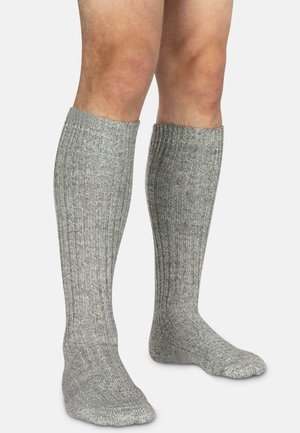 Beine tragen knielange, gerippte, graue Stricksocken auf einem schlichten hellen Hintergrund, die die detaillierte Textur des Stoffes zeigen.