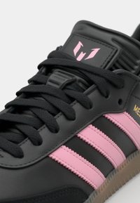 Sort lædersneakers med pink striber, gummisål, runde snørebånd og et logo på tungen. Har teksturerede detaljer og et strømlinet design.