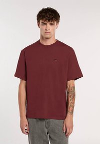 T-shirt bordeaux in cotone con scollo rotondo e maniche corte. Presenta un piccolo logo del marchio sul petto. Tessuto morbido, vestibilità comoda.