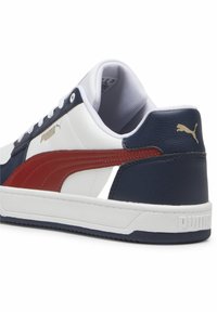 Zapatilla blanca con acentos en azul marino y rojo, materiales de cuero y sintéticos, cuello acolchado, suela de goma y detalles del logo en dorado en el lateral.