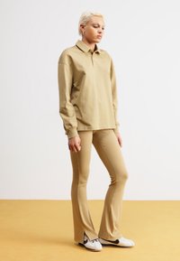 Polo shirt beige a maniche lunghe abbinato a pantaloni beige a zampa d'elefante. Sneakers bianche con dettagli neri. Design semplice, texture liscia e vestibilità casual.