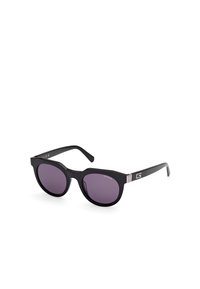 Ochelari de soare supradimensionați, negri, cu un finisaj lucios, lentile violet și accente argintii pe bradă, având înscris numele brandului "GUESS."