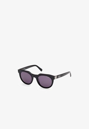Gafas de sol de gran tamaño en negro con acabado brillante, lentes morados y detalles plateados en las varillas que presentan el nombre de la marca "GUESS."
