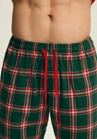 Zielone flanelowe spodnie do piżamy w czerwono-biały wzór kratki. Posiadają elastyczny pas i czerwony sznurek. Miękka tekstura materiału.