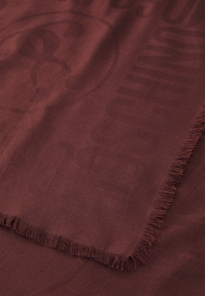 Tecido vermelho escuro com símbolos, letras e bordas franjas tecidas de forma subtil, apresentado em close-up.