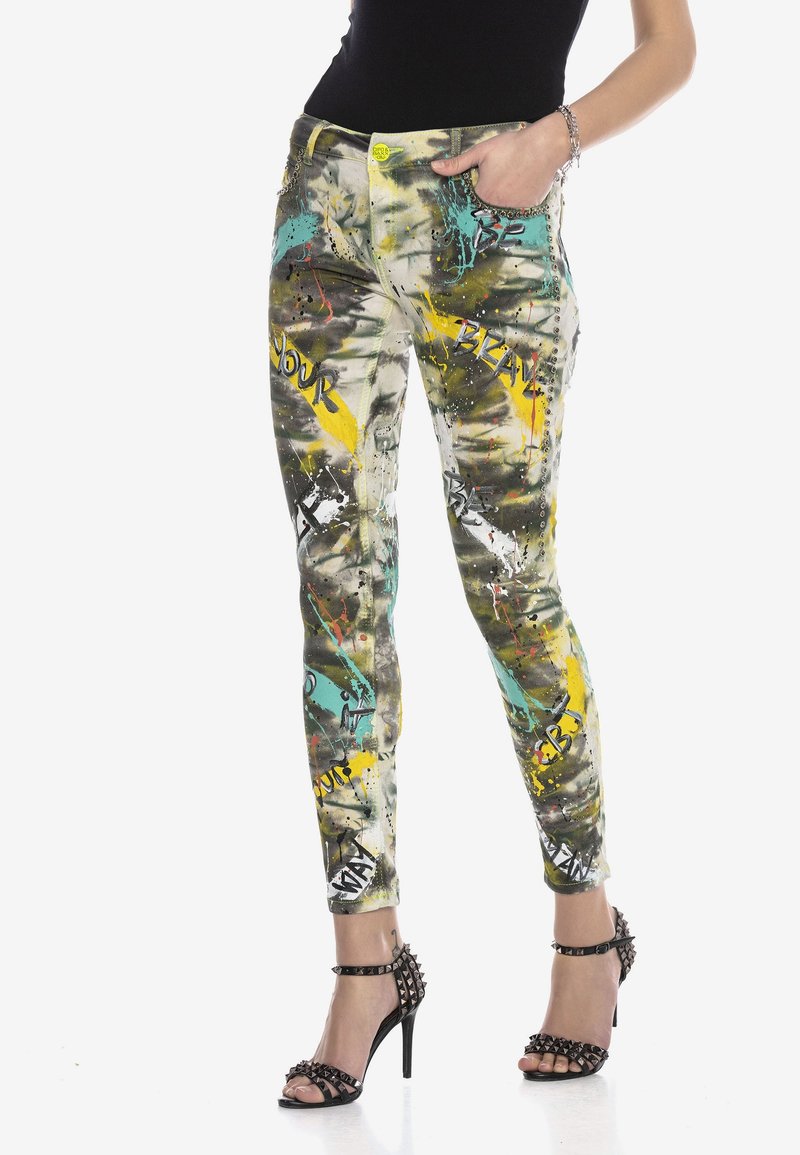 Jean skinny multicolore ajusté avec un design éclaboussé de peinture comprenant des accents jaunes, sarcelle et noirs. Taille haute avec des détails en métal.