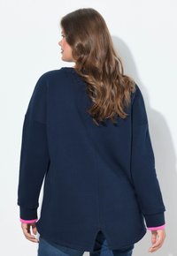Felpa blu navy con vestibilità ampia, caratterizzata da dettagli rosa sui polsini, orlo arrotondato e schiena con spacco. Tessuto morbido.