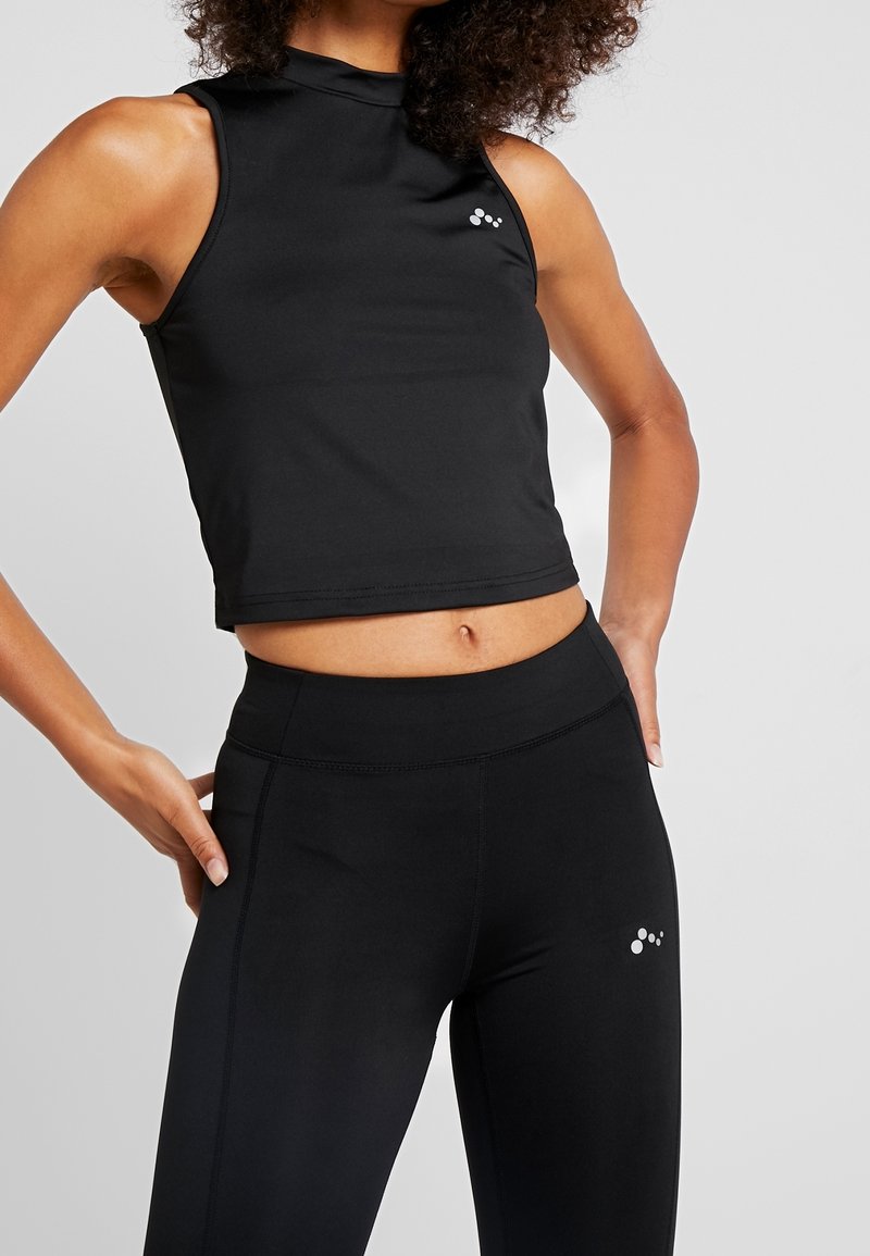 Débardeur de sport noir à col montant et sans manches, associé à un legging taille haute assorti, orné d'un petit logo.