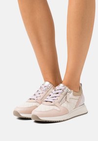 Light pink sneakers with a quilted pattern and metallic accents. Features a lace-up front, zipper on the side, and a cushioned sole.