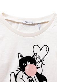 Colletto di una camicia bianca con una grafica di un gatto bianco e nero che soffia una gomma da masticare rosa e tiene un palloncino a forma di cuore legato con un fiocco.