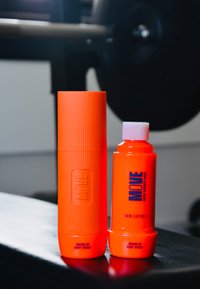 Oranje cilindrische container met ribbelstructuur, gelabeld "MOVE" en "WARM-UP BODY SPRAY"; kleinere oranje fles ernaast, ook gelabeld.