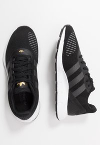 Svarta sportskor av andningsbart stickat material, med grå ränder och accenter, vit mellansula och texturerad yttersula.