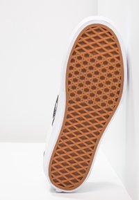 Sneakerzool met een witte rubberen rand, een oranje gestructureerd grippatroon en een zwart logo-accent aan de zijkant.