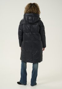 Abrigo acolchado negro con capucha, con un diseño acolchado y de larga longitud. Material texturizado con un acabado brillante y un corte relajado.