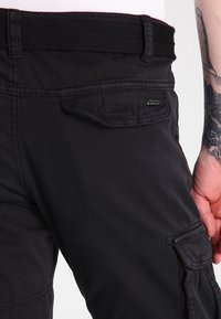 Zwarte cargobroek met een textuur elastische tailleband, zijzakken en een klein merklabel op de achterzak.